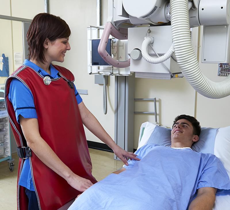 female x-ray tech wearing Luxel dosimeter badge for radiation monitoring and lead apron with patient in hospital